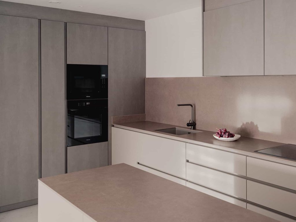 Una cocina que invita al diálogo La zona de la cocina ha sido equipada con una isla abierta para dar continuidad a la sala de estar, estableciendo así un diálogo entre los dos espacios. Se logra calidez y elegancia mediante la madera y el uso de materiales innovadores como el Corian utilizado en las encimeras.Ampliar